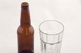 Brown unlabeled bottle of beer with an empty glass on a white background, close up high angle view