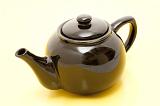 Brown glazed ceramic teapot with a closed lid on a white background with a colorful yellow brown shadow reflected off the glaze