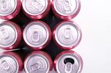 Canned drinks background with an overhead view of nine neatly arranged red aluminium cans with only one with an open tab, on white with copyspace