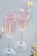 Two festive romantic glasses of pink champagne in elegant flutes with gold party streamers to celebrate a special occasion