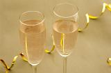 Two flutes of golden bubbly champagne at a romantic party celebration with a diagonal twirled gold streamer behind, close up high angle view