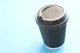 Coffee to go in a plastic disposable cup with a closed lid, high angle view on a turquoise blue background