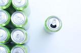 Green aluminium drink cans neatly arranged in rows with a single can to the right that has been opened, overhead view on white with copyspace