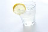 Gin and tonic on ice with lemon in a plain glass tumbler for a refreshing alcoholic beverage on a white background