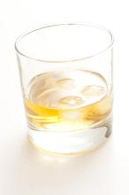 Glass of whiskey or scotch with ice cubes, close-up on white