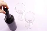 Close up of the hand of a man opening a bottle pf red wine to pour it into two wineglasses, high angle view on white