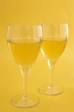 Two wineglasses of white wine standing side by side on a yellow background