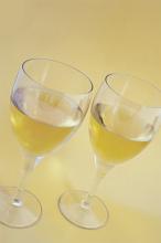 Two glasses of white wine standing side by side, high angle view over a pale yellow background with copyspace