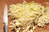 Sliced raw cabbage on a chopping board with a sharp kitchen knife ready to be used in a coleslaw salad or cooked for a meal