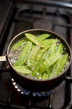 Cooking mangetout peas in a pot of boiling water on a gas hob, high angle view