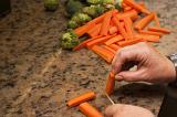 Cook cutting and cleaning fresh raw vegetables preparing carrot batons and broccoli, close up of his hands