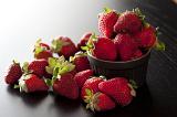 Fresh ripe red strawberries in a ramekin overflowing onto the surface below with side lighting, copyspace and shadow