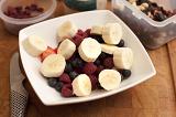 Healthy dessert of fresh fruit in a bowl with a mixture of raspberries, strawberries, and blueberries topped with sliced banana on a wooden table