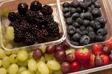 Punnets of fruit and berries with fresh juicy green and purple grapes, youngberries or blackberries, blueberries and strawberries, high angle view
