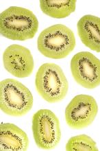 Kiwifruit background pattern and texture with thin slices of peeled fruit arranged randomly on a white background, overhead view