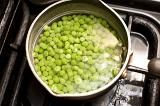 Pot of fresh green peas on the hob standing in water waiting to be cooked and boiled as an accompaniment to a meal