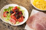 Cold lunch of fresh mixed salad with lettuce, tomato and olives served with a plate of sliced cured ham