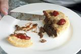 Man eating a pastry meat pie topped with tomato ketchup cutting it with a knife, close up view