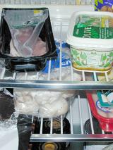 Contents of refrigerator with various groceries in commercial and home packaging on wire metal shelves