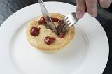 Fresh meat pie with a smiling face formed of sauce on the pastry crust being cut into with a knife and fork for lunch