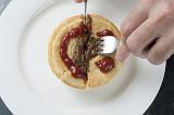 Man cutting open a tasty meat pie with a cute gravy face on top of the pastry using a knife and fork as he prepares to eat it for lunch, high angle close up view