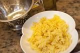 Plate of plain cooked Italian spiral pasta standing on a kitchen counter alongside a metal colander for draining it