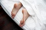 Man lying in bed on a lazy day with his feet sticking out the bottom of the bed from under the white bedclothes, close up view