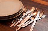 Loose cutlery and a stack of empty plates on a buffet table with knives, forks and spoons on a wooden tabletop