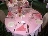 Elegant formal dining table with pink decor at a catered event or reception set with stylish linen, silverware and glassware, high angle view