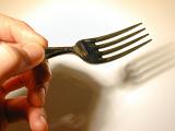 Close up of the fingers of a man holding a fork casting a shadow onto a white plate