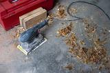 Electric sander and red toolbox on a woodworking workshop floor with scattered wood shavings and copyspace