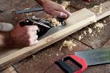 Man planing a length of wood by hand using a handheld plane with an adjustable blade in a DIY and renovation concept