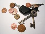 A bunch of house and car keys with scattered coins and a single brown button lying in random array on a grey surface