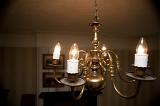 Illuminated brass chandelier with classic candle-style arms hanging from the ceiling in a darkened room