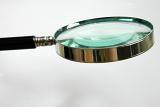 Magnifier with thick lens, metallic frame and black plastic handle, tool used in research, investigations and detailed observations for increased view, close-up with copy space on gray