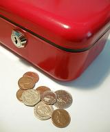Red metal cash box with a lock and loose coins lying alongside it, closeup high angle view of the corner
