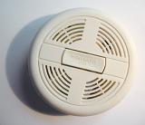 Round white plastic cover of a smoke detector on a wall or ceiling to warn of a fire hazard, close up view