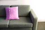Pink cushion on a comfortable upholstered grey sofa, close up view against a white wall with copyspace