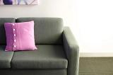 Pink cushion with button decoration on a comfortable neutral couch or settee against a white wall in daylight