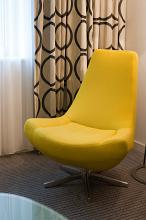 Retro style elegant yellow bucket chair standing in front of a window with bold patterned floor length drapes