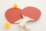 Two colorful red wooden ping pong or table tennis bats lying crossed over on a white background with two loose yellow balls alongside