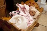 Tight view of cute little blond doll wrapped in blankets laying down in wooden crib on floor