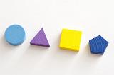 Four different shaped wooden toy blocks laid out on a white background with a circle, triangle, square and pentagon