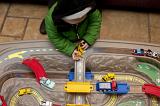 High Angle View of Unrecognizable Young Boy Wearing Winter Coat Playing with Toy Cars on Mat with Roads and Varying Terrain