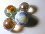 Collection of four different childhood glass marbles casting creative shadows over a grey background with copy space