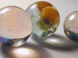 Three glass toy marbles in clear and brown swirling designs and different sizes with shadows over gray background