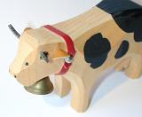 Wooden toy cow with a brass bell on a red band around its neck and leather ears viewed close up high angle