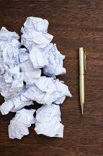 Concept of bad or unworkable ideas with a heap of crumpled white note paper on a desk with a pen
