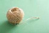 Small clew of jute threads of natural linen or ball of rustic strings viewed in close-up on pale green background