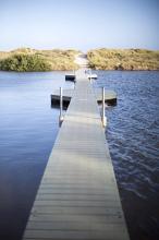 Long wooden boardwalk bridge over the water of a lake stretching straight ahead in a concept of crossing bridges